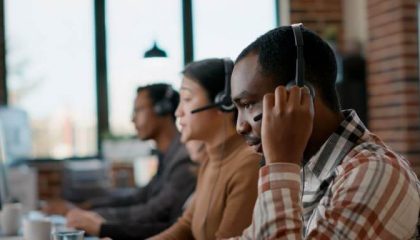 Male worker answering telework phone at call center, using audio headset and microphone. Young man working at customer care in disability friendly office. Handheld shot. Close up.