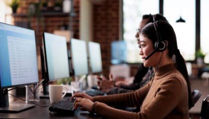 Paralyzed asian employee working at call center reception in disability friendly office. Female operator wheelchair user with impairment giving assistance on customer service helpline.